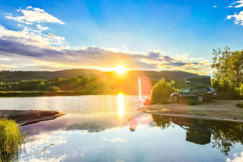 auto mit dachzelt am ufer eines sees bei sonnenuntergang