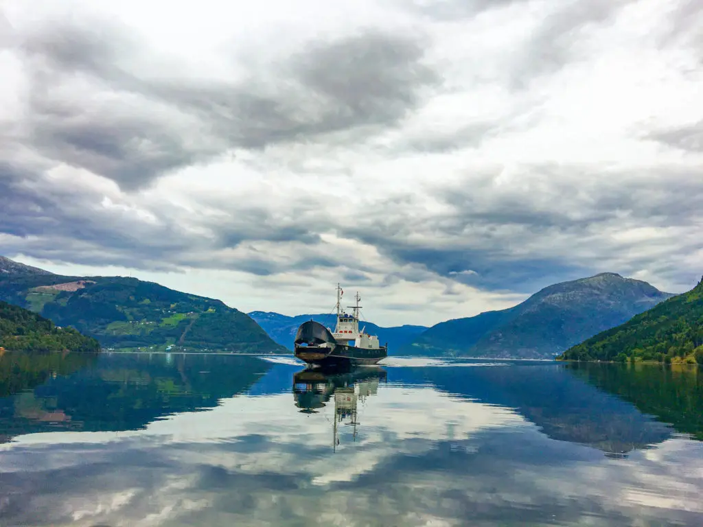 Fähre auf einem Fjord umgeben von Bergen und Wald