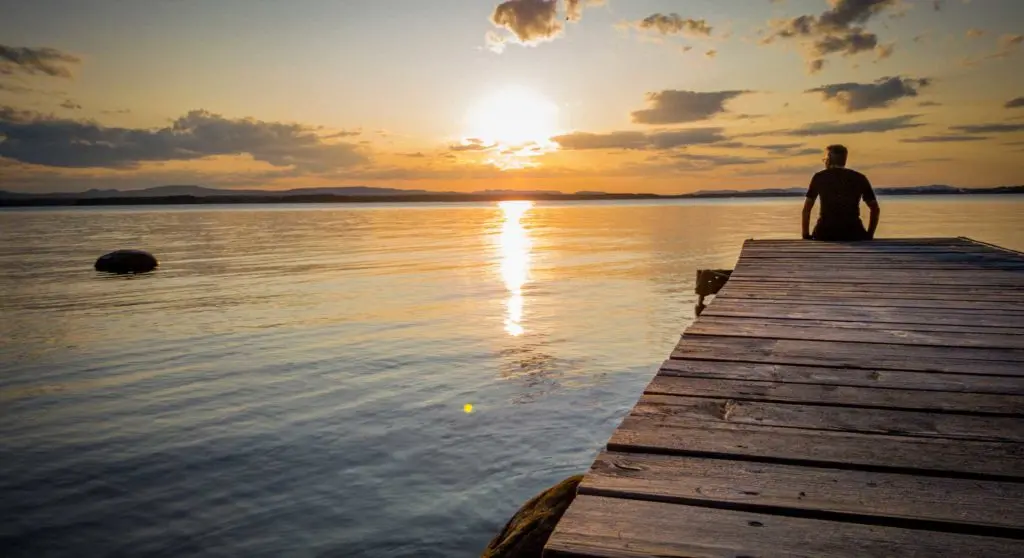 mann auf einem holzsteg sonnenuntergang wasser