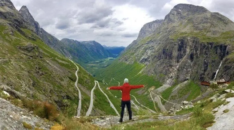 Mensch mit roter Jacke und mütze in grüner natur fjord in norwegen trollstigen