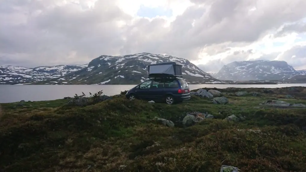 Auto mit Dachzelt an einem See mit Bergen im Hintergrund