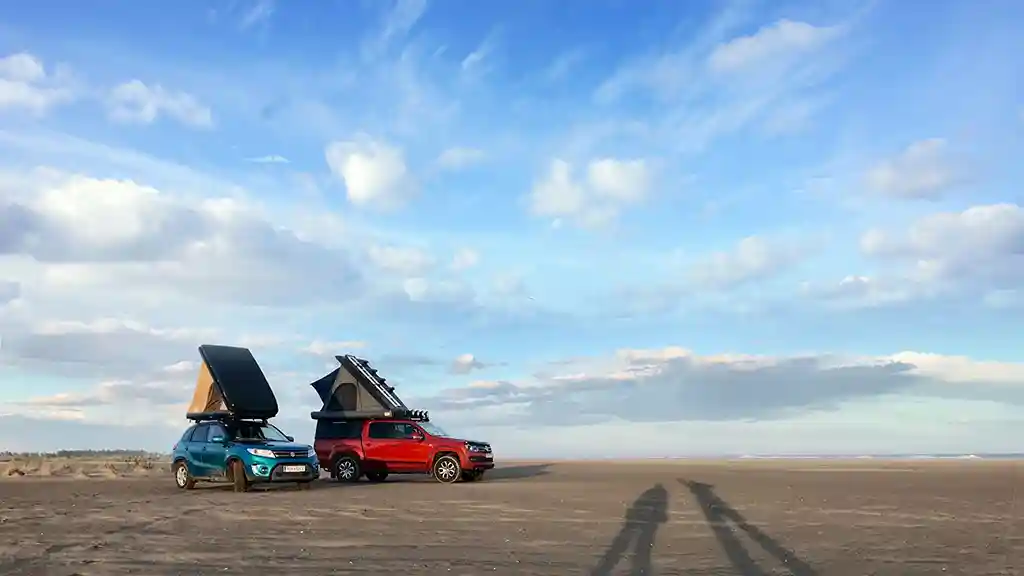 dachzelt finden dachzelt leihen mieten Hartschalendachzelte dreieckig auf einem roten und einem türkisfarbenen auto sand blauer himmel