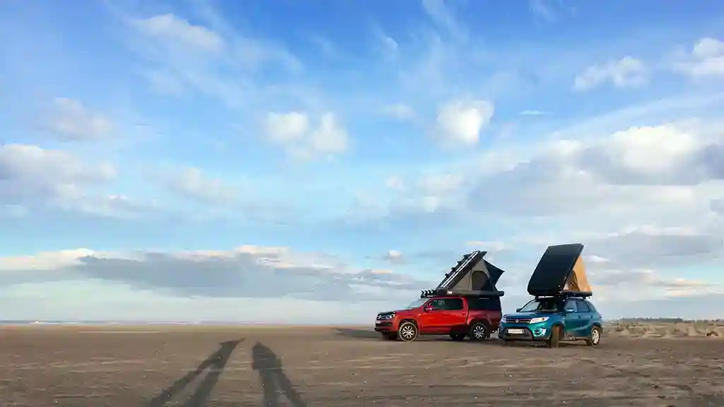 Dachzelt leihen Private Dachzelt Vermietung Hartschalendachzelte dreieckig auf einem roten und einem türkisfarbenen auto sand blauer himmel