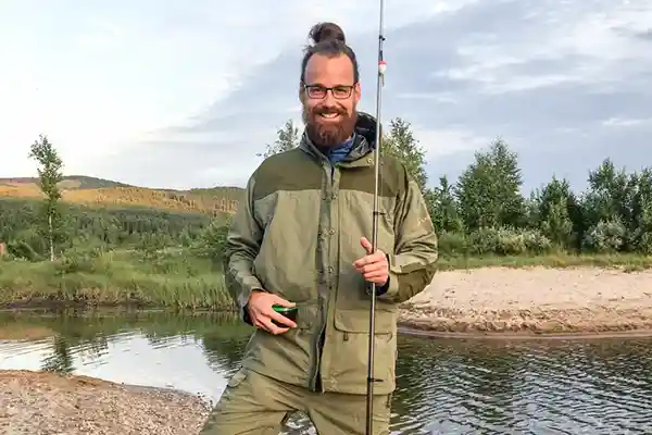 Mann mit Angel an einem See mit Wald im Hintergrund angeln in Norwegen