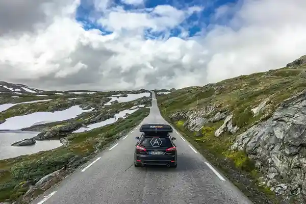 schwarzes Auto mit Hartschalendachzelt zusammengepackt alleine auf der Strasse schneeflecken grün wolken am himmel