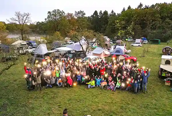 Luftaufnahme gruppenfoto dachzeltnomaden menschen im vordergrund autos mit dachzelten im hintergrund