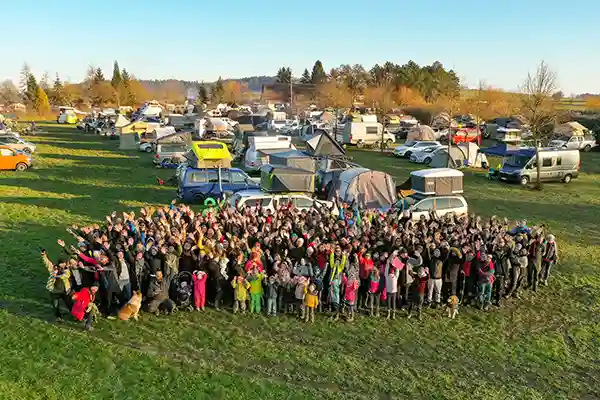 Menschen auf einer Wiese im Vordergrund Dachzelte auf Autos im Hintergrund