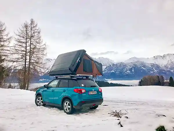 wintercamping suzuki ikamper hybriddachzelt schnee kahle baeume bergkette