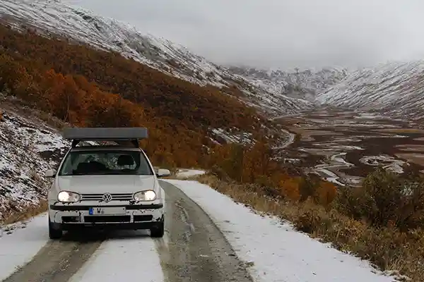 weisses auto zusammengefaltetes dachzelt schnee buesche gras weite strasse