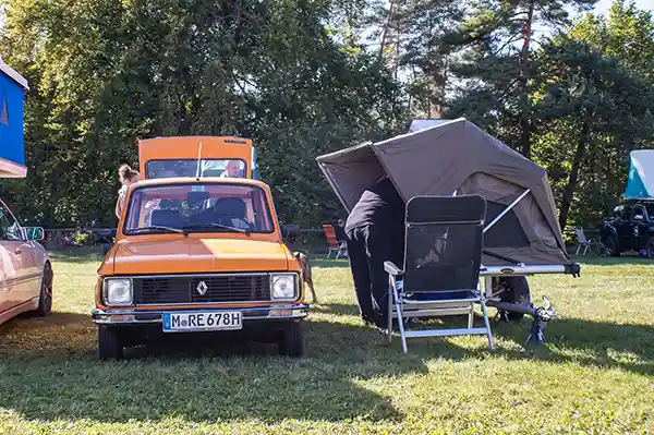 oranges Auto mit schwarzem Klappdachzelt auf einem Anhänger