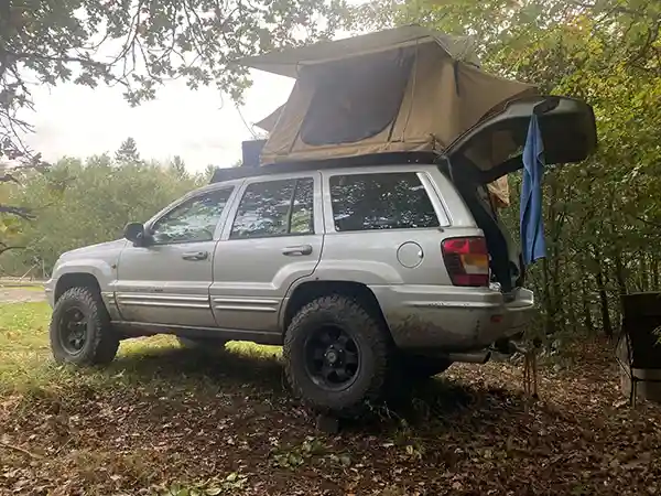 Geländewagen mit Klappdachzelt unter bäumen