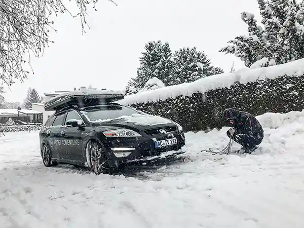 schneeketten anlegen mann auto schnee winterlandschaft winter