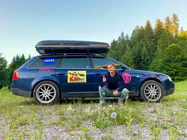 Frau vor Auto mit Dachzelt wiese blauer himmel baeume