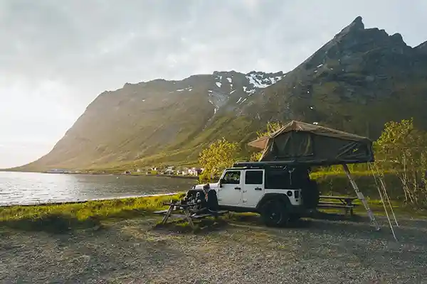 Auto mit dachzelt an einem see mit bergen im hintergrund