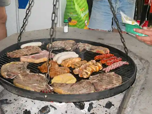 schwenkgrill mit würsten fleisch und burgern über dem feuer