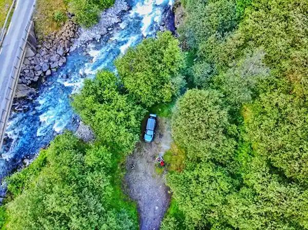 Auto mit dachzelt in grünem Wald mit Fluss in Norwegen