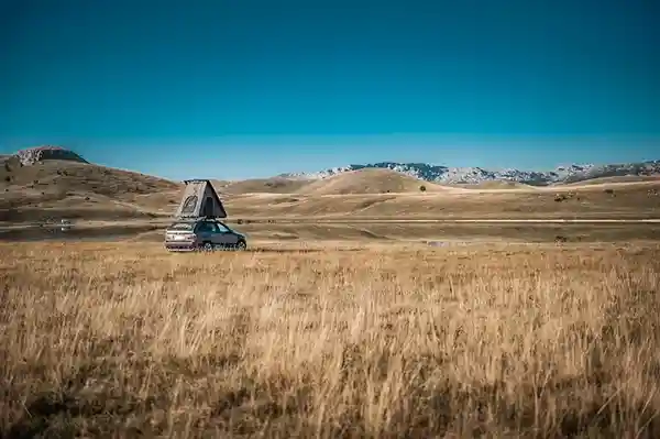 Dreieck Hartschalendachzelt auf einem Auto in einer Wiese, blauer himmel weite aussicht